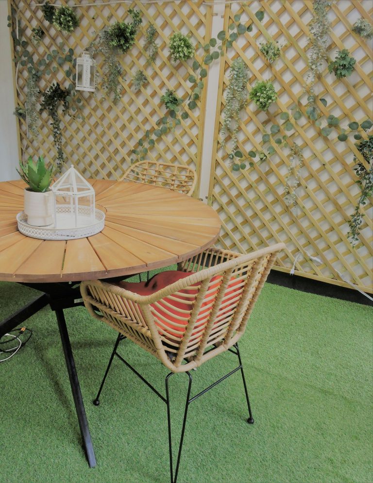 A stylish patio with a wooden table and rattan chair, perfect for outdoor relaxation.